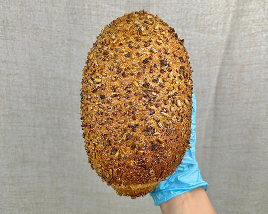 Loaf of bread with seeds held by a gloved hand against a neutral background